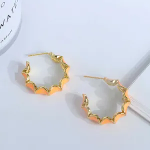 Détail de boucles d'oreilles créoles dorées avec bords ondulés et émail orange vif