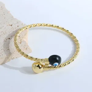 Detail of 18K gold plated twisted rope cuff bracelet with black enamel evil eye charm