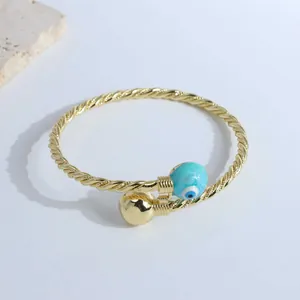 Detailed shot of twisted rope gold cuff bracelet featuring evil eye bead and gold ball charm
