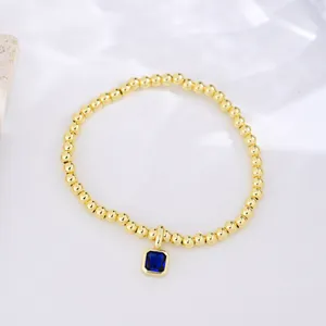Macro detail of 18k gold plated beaded bracelet with blue square zircon birthstone charm