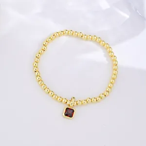 Detail of 18k gold beaded bracelet featuring a square red zircon birthstone pendant