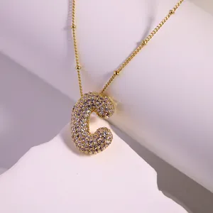 Gold plated micro-pave zircon letter C necklace with beaded chain on white pedestal