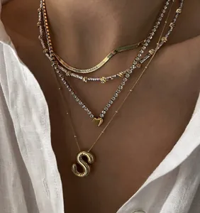 Close-up van gelaagde gouden kettingen met hart en 'S' hangers op een wit shirt