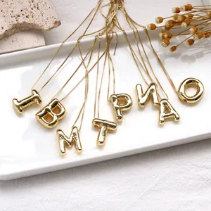 Polished gold balloon initial pendants with box chain on a white display tray