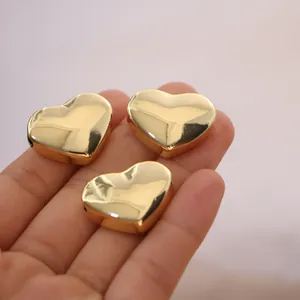 Three 18K gold heart-shaped metal spacer beads with polished mirror finish on hand