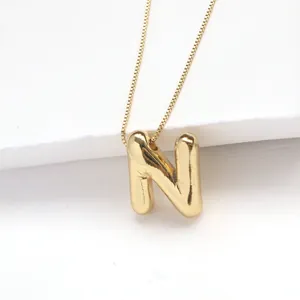 Macro detail of a 3D bubble letter N pendant on a gold box chain against white background