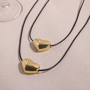 Detailed view of dual 18K gold-plated heart pendants on black wax cords over a beige surface