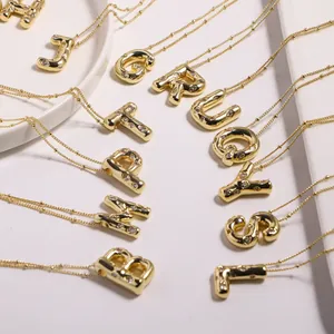 Detail of gold letter necklaces with sparkling zircons and fine ball chains on ceramic