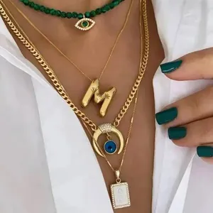 Layered gold necklaces with balloon letter M, evil eye pendants, and green beads on a model
