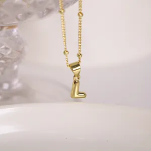 Macro shot of 18K gold letter L pendant on a delicate beaded satellite chain necklace