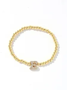 Close-up of golden beaded elastic bracelet with a sparkling crystal letter E charm