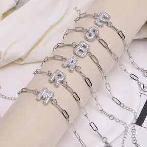 Bracelet chaîne trombone argentée avec lettres en zircons sur un support beige