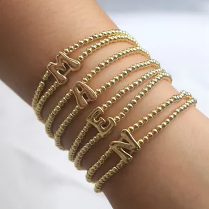 Detail von goldenen Perlenarmbändern mit metallischen Buchstabenanhängern im Ballon-Stil