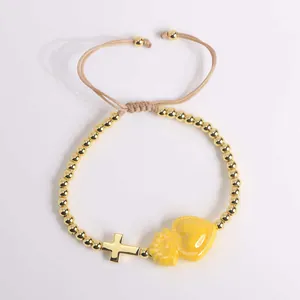 Detail of 18K gold beaded bracelet featuring a cross pendant and yellow enamel heart charm