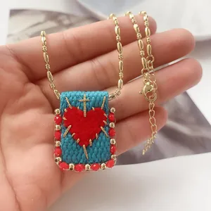 Macro shot of 18K gold woven square pendant necklace featuring a red heart and golden cross