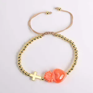 Detail of 18K gold beaded bracelet with cross and orange heart pendant on cord