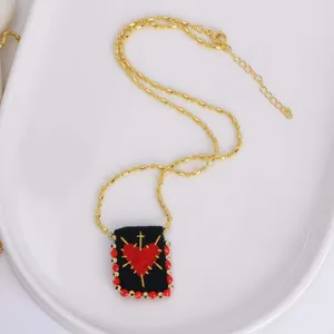 Macro detail of 18K gold chain and handwoven square pendant with cross and heart