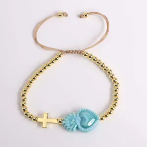Detail of beaded bracelet with blue sacred heart and gold cross on a woven cord