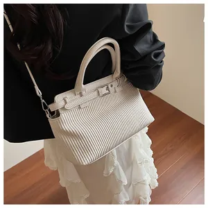 Detail of cream pleated crossbody bag with silver buckle and leather strap on model