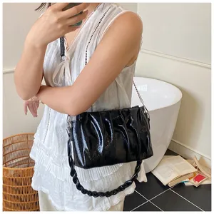 Detail of black pleated cloud bag with braided handle and metal chain on a model