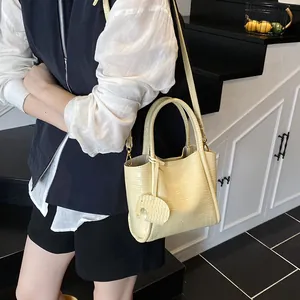 Sac seau jaune crème à motif crocodile avec pendentif éléphant porté par mannequin