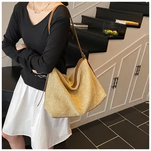 Detailed view of large woven straw tote bag with brown straps and zipper detail on model