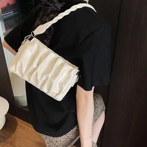 Chic beige pleated cloud shoulder bag with woven strap and shiny finish on a model