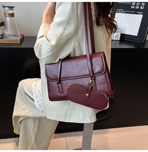 Detail van bordeauxrode leren schoudertas met bijpassende mini-etui op model