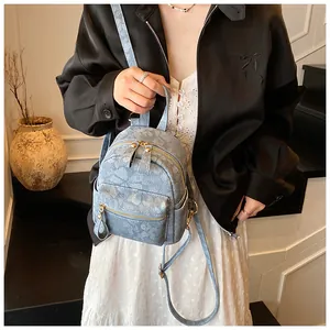 Close-up of light blue floral mini backpack with golden zippers held by a model