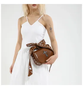 Detail of studded bow handle and vintage metal cross on dark brown glossy handbag