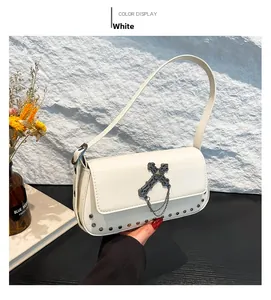 Close-up of white crossbody bag with silver cross charm and metal chain details