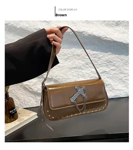 Detail view of brown glossy leather shoulder bag with cross pendant and metal rivets