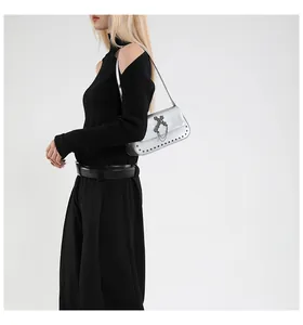 Silver square crossbody bag with metallic studs and cross detail worn by a model