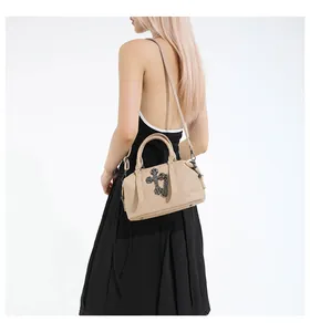 Bolso bandolera en cuero granulado beige con aplique de cruz negra y correa larga