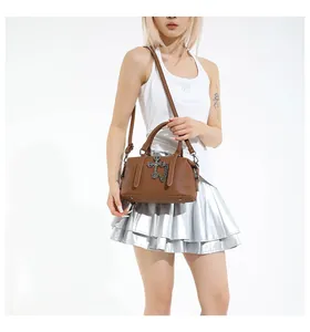 Bolso tote de cuero granulado marrón con cruz plateada y cadena llevado por modelo