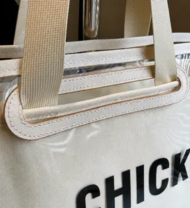 Gros plan des coutures renforcées sur les poignées en sangle crème d'un sac cabas transparent
