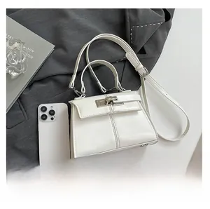 Detailed view of white trapezoid handbag with metal lock and smartphone for size reference