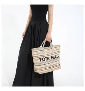 Détail d'un grand sac cabas en paille à rayures avec broderie porté par un modèle