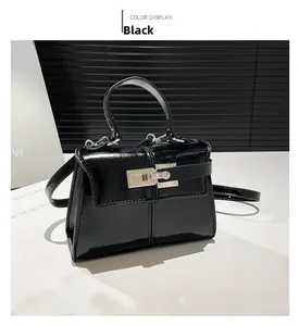 Detail view of black glossy patent leather handbag with metal buckle and top handle design