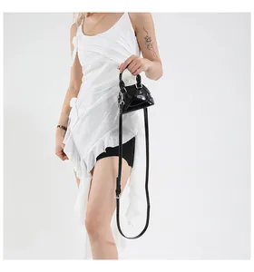 Mini sac coquille en cuir verni noir avec détails argentés porté par un mannequin