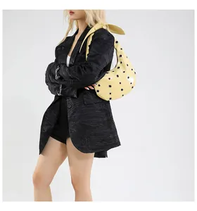 Detail of yellow patent leather shoulder bag with silver eyelets and knotted strap detail