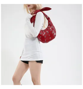 Detail view of a dark red glossy shoulder bag with silver metal grommets on a model