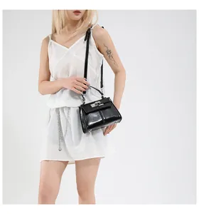 Glossy black trapezoid handbag with silver lock and shoulder strap worn by a model