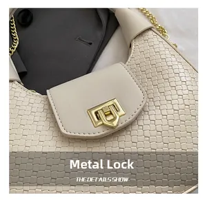 Detail view of the golden hardware lock and woven texture on a cream shoulder bag
