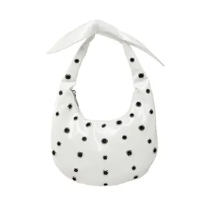 White hobo shoulder bag with silver eyelets and a large decorative bow on strap