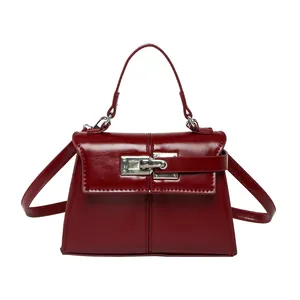 Deep red patent leather trapezoid handbag with metal clasp and adjustable shoulder strap