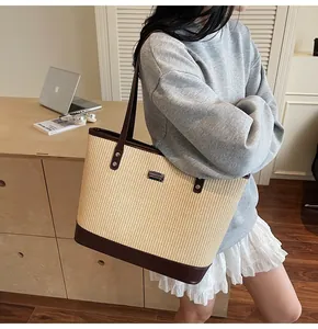 Detail of large woven straw tote bag with brown leather handles and silver metal logo plate