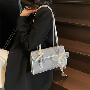 Light blue underarm bag with ribbon bows and wood grain texture worn over a black blazer