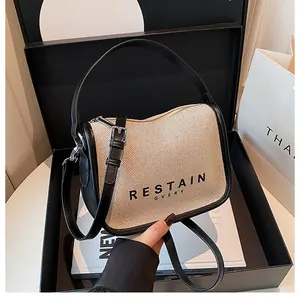 Close-up of beige knit bag with black leather trim and letters in a gift box setup