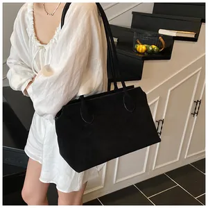 Minimalist black matte tote bag detail shown on shoulder with elegant pleated top outfit